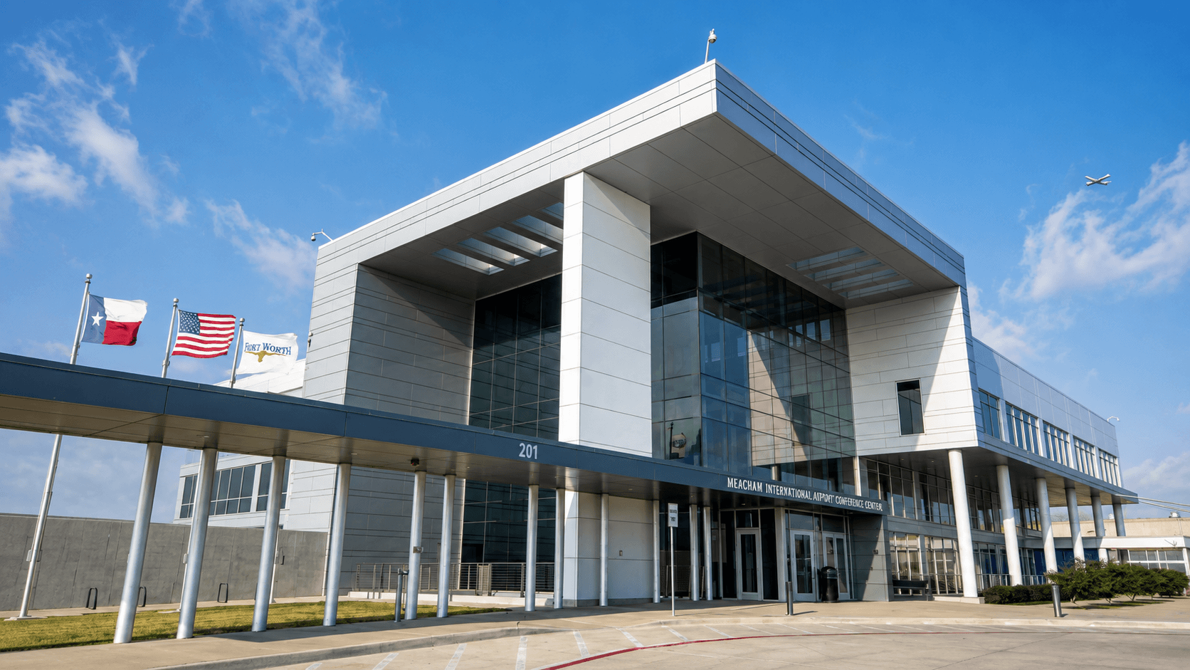 The exterior of Meacham International Airport Conference Center in Fort Worth — a glass and steel building under a blue sky, with a light aircraft overhead.