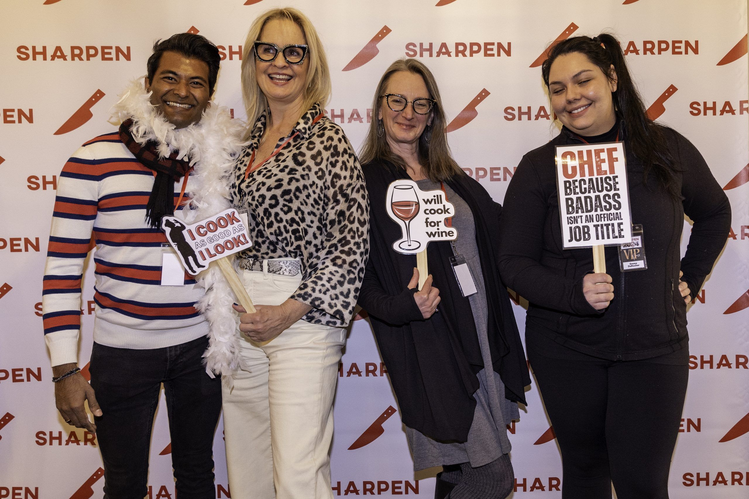 Four attendees posing with props at the SHARPEN backdrop.