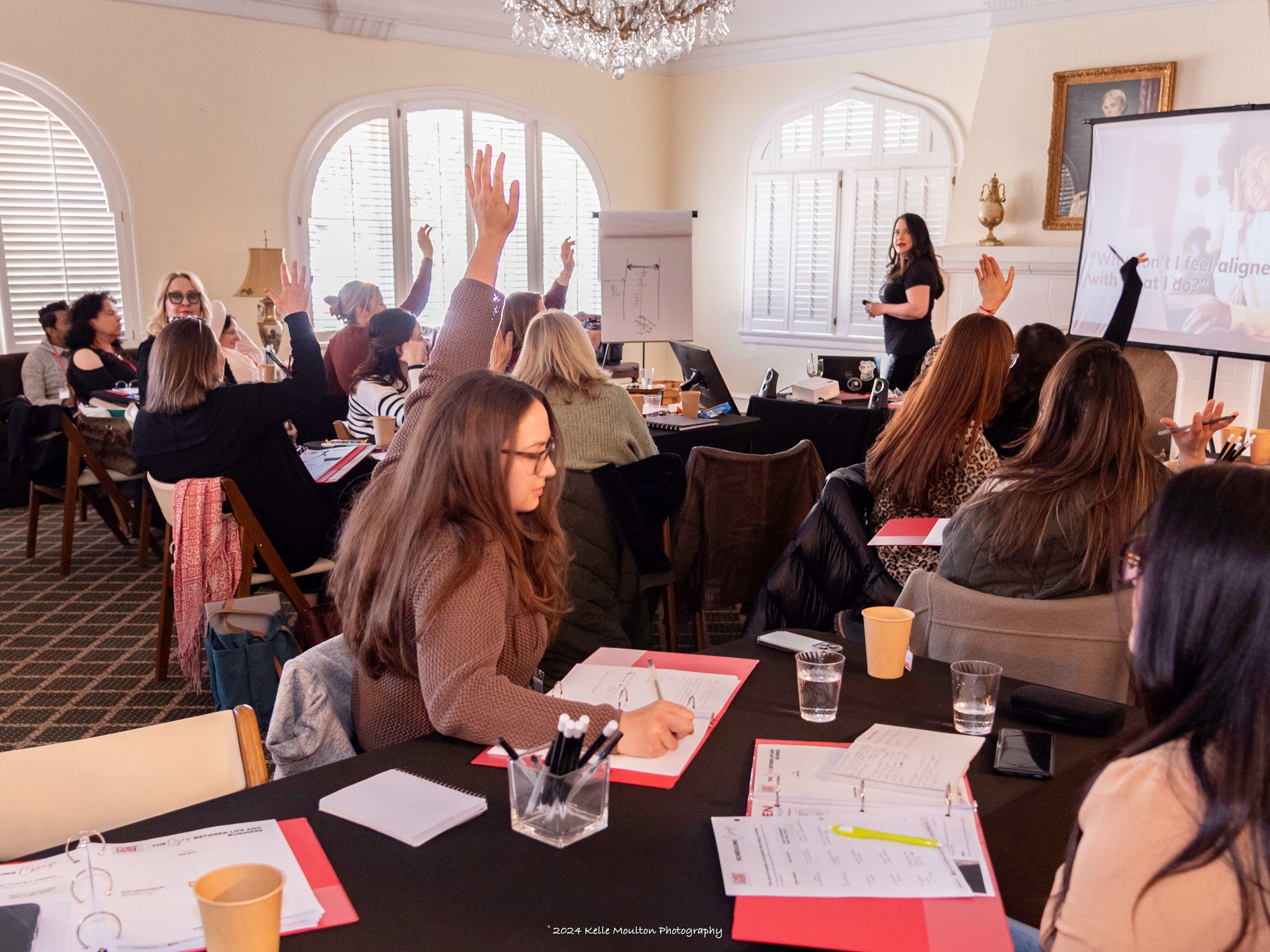 A full room of culinary business owners at SHARPEN, seated at long tables with worksheets, several hands raised, Chef Deb at the front.